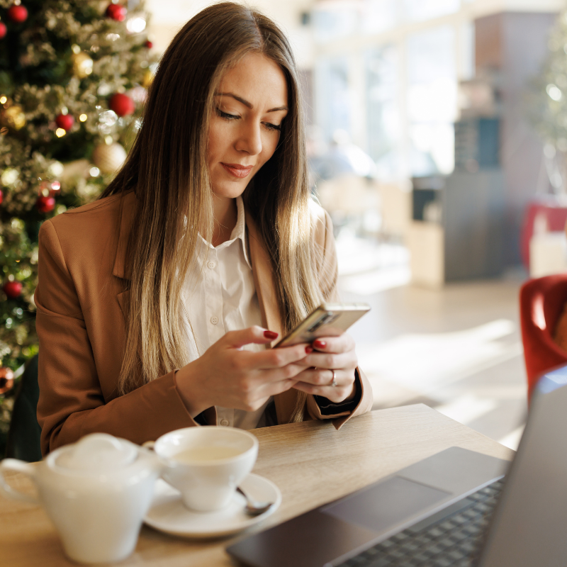 woman messaging on phone around holiday decor